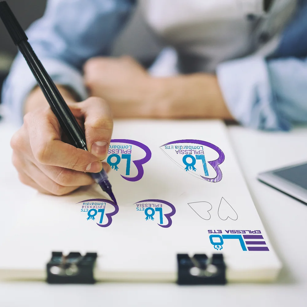 Mano che disegna varianti del logo ELO Epilessia su blocco note — progettazione logo Milano